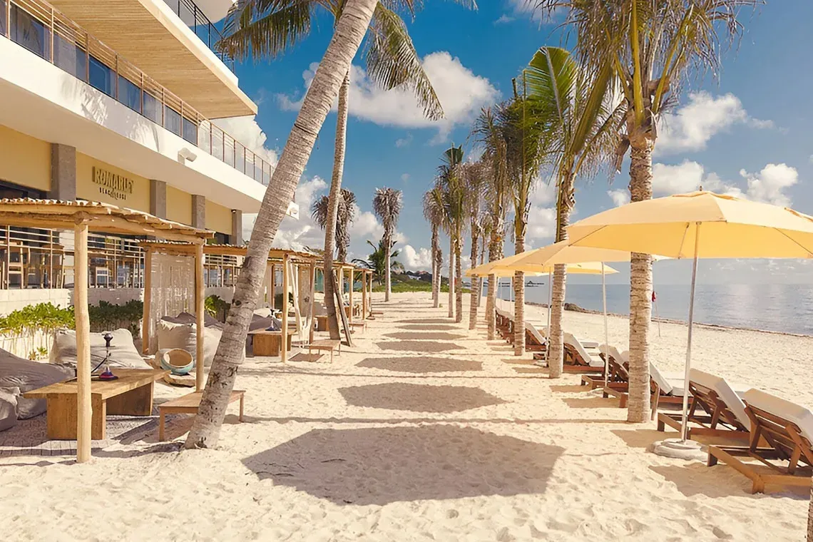 The Fives Corpo: Mexican beach with palm trees, loungers, and cabanas.