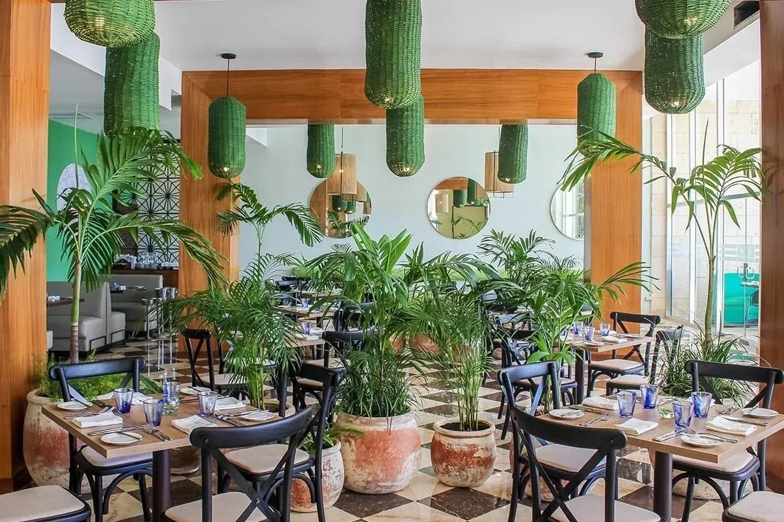The Fives Corpo restaurant: tables with lush plants and green pendant lights.