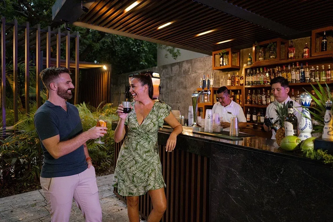 Pareja disfrutando cócteles en el bar de The Fives Beach Hotel - Á la Carte All Inclusive | México | Web oficial.