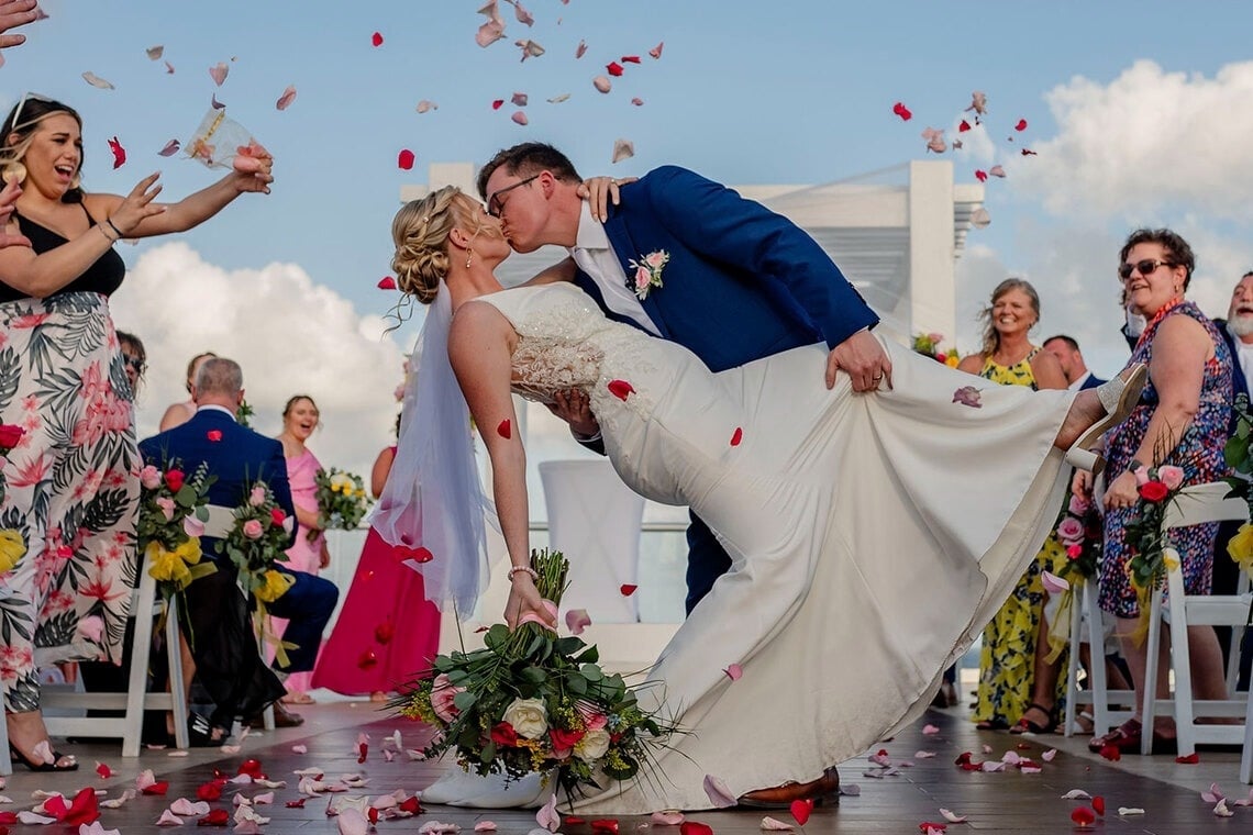 a bride and groom walking on the beach at sunset