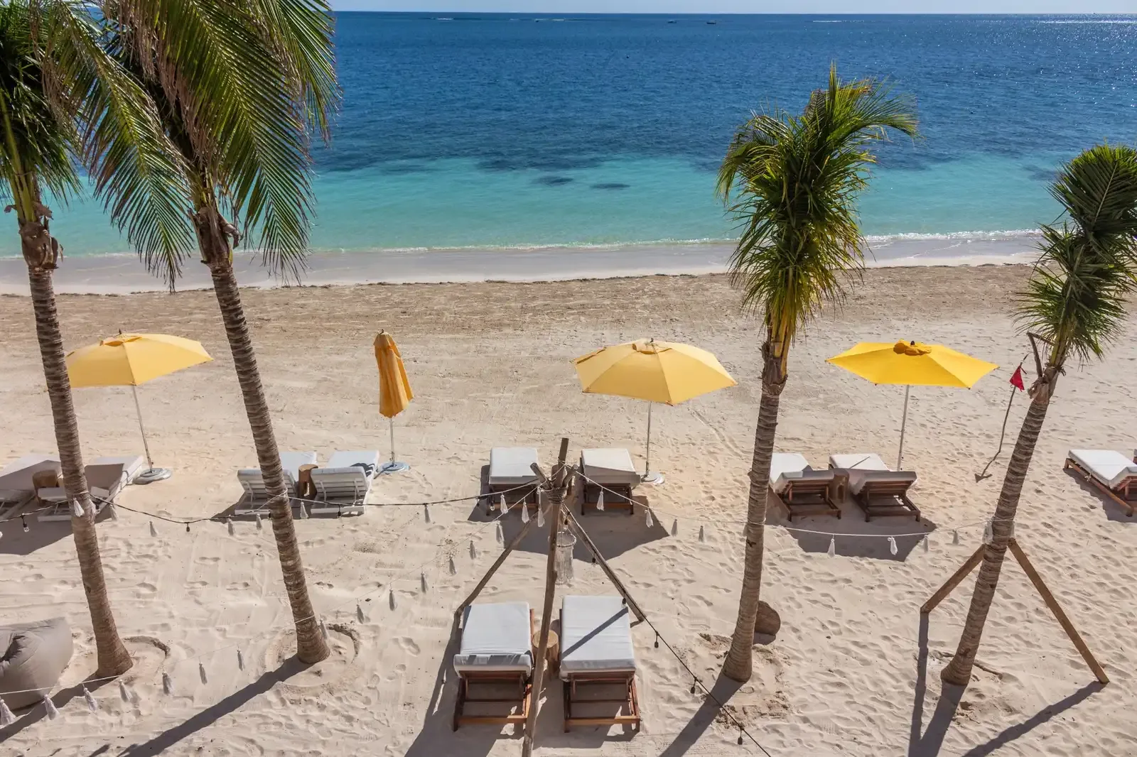 Tropical beach resort with lounge chairs, yellow umbrellas, and palm trees. The Fives Corpo
