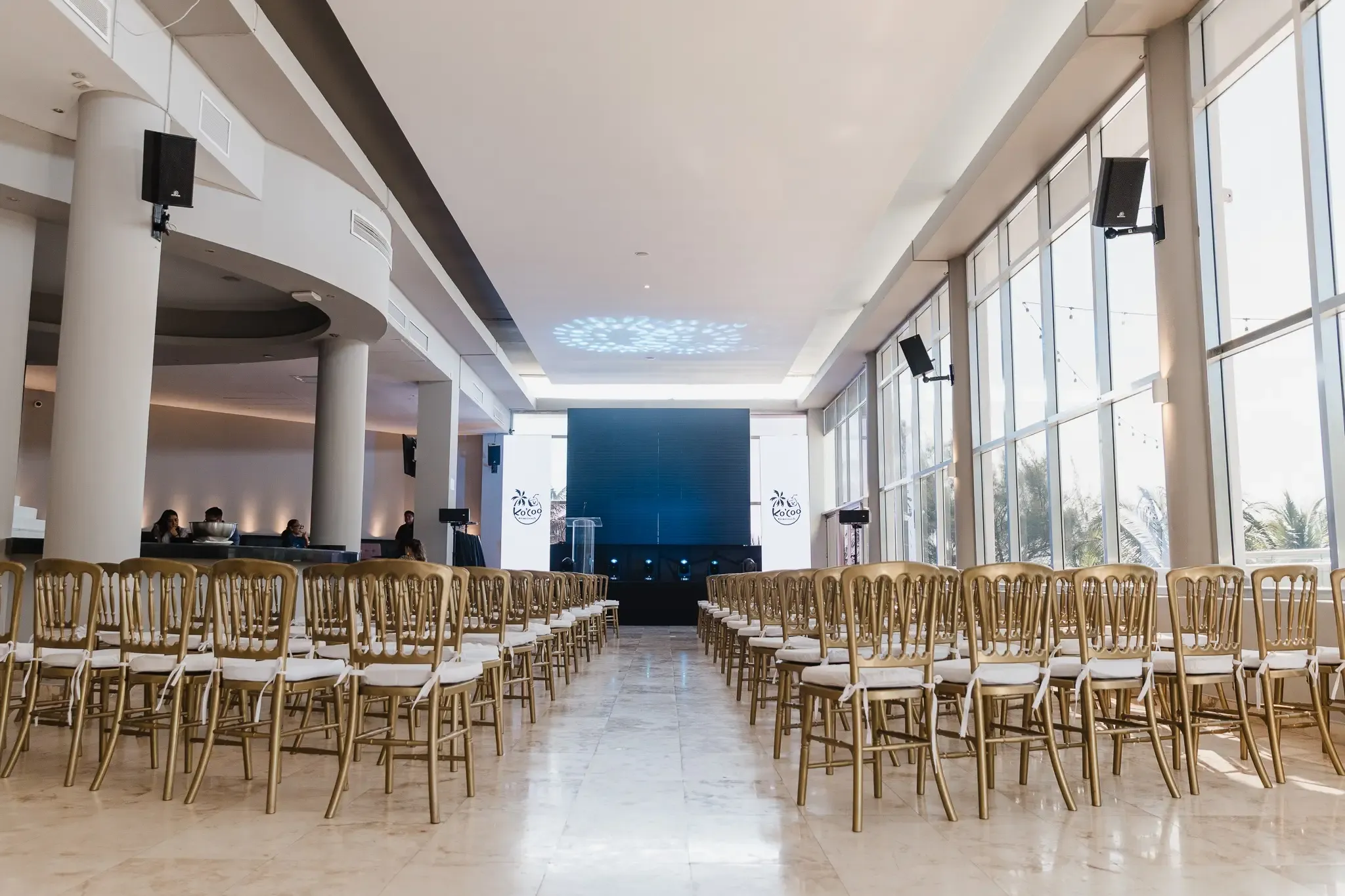 Chairs set up for an event in a hotel ballroom with large windows and a stage, perfect for your next The Fives Corpo.