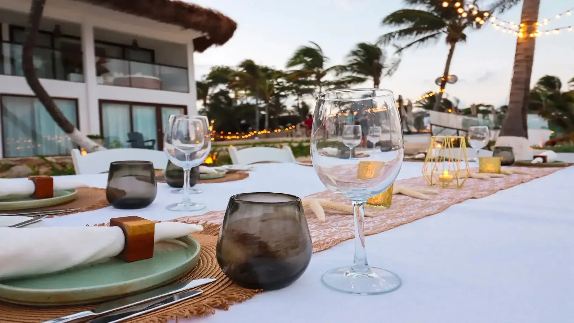 Elegant beachfront dining setup for events, featuring tableware and palm trees. Events | The Beachfront by The Fives Hotels | Official website.