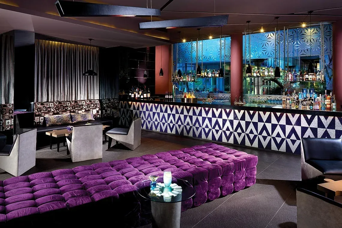 Lounge moderno de The Fives Corpo con asientos morados y barra.