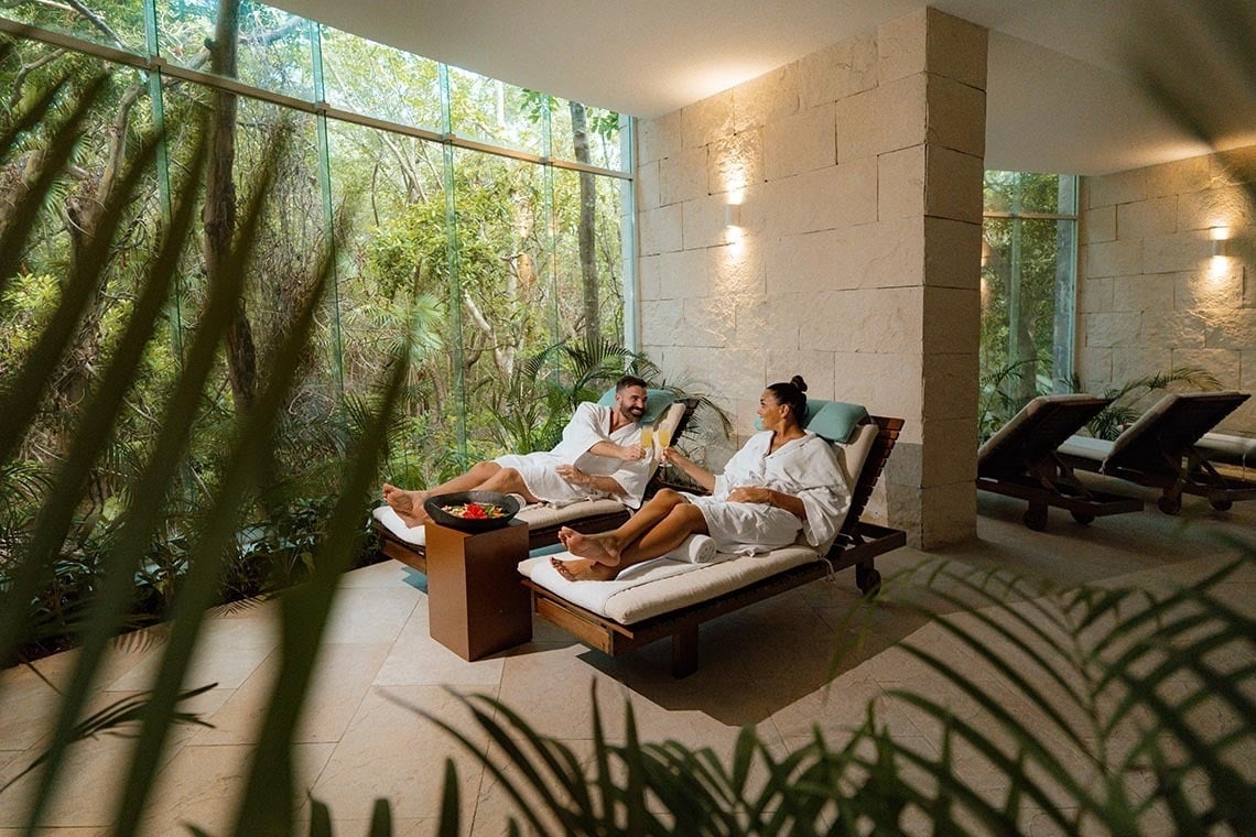 The Fives Beach Hotel: Couple relaxes in robes with drinks, jungle view.