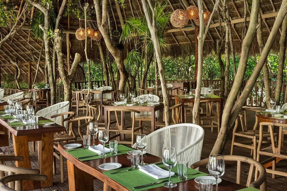Restaurante al aire libre con mesas y sillas de madera en The Fives Hotels, rodeado de árboles.