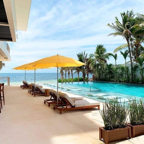 a swimming pool surrounded by chairs and umbrellas with the ocean in the background