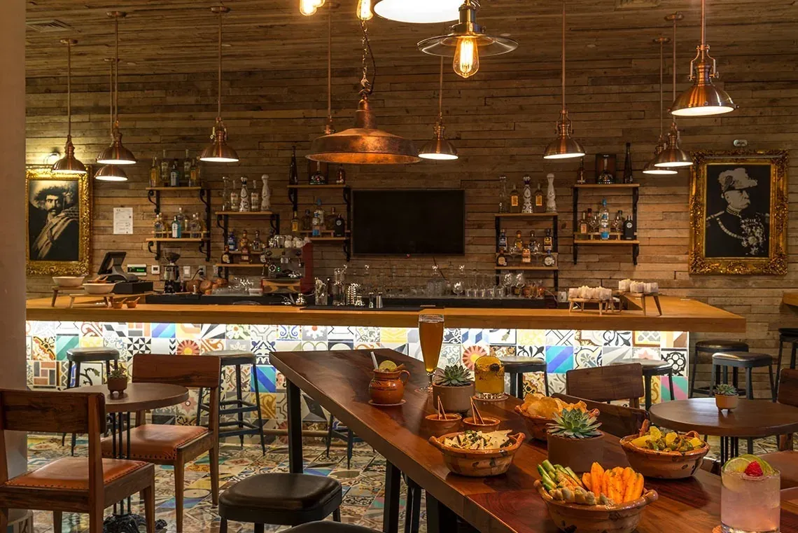 Bar y restaurante temático de The Fives Corpo con decoraciones de madera, botellas de tequila y arte.