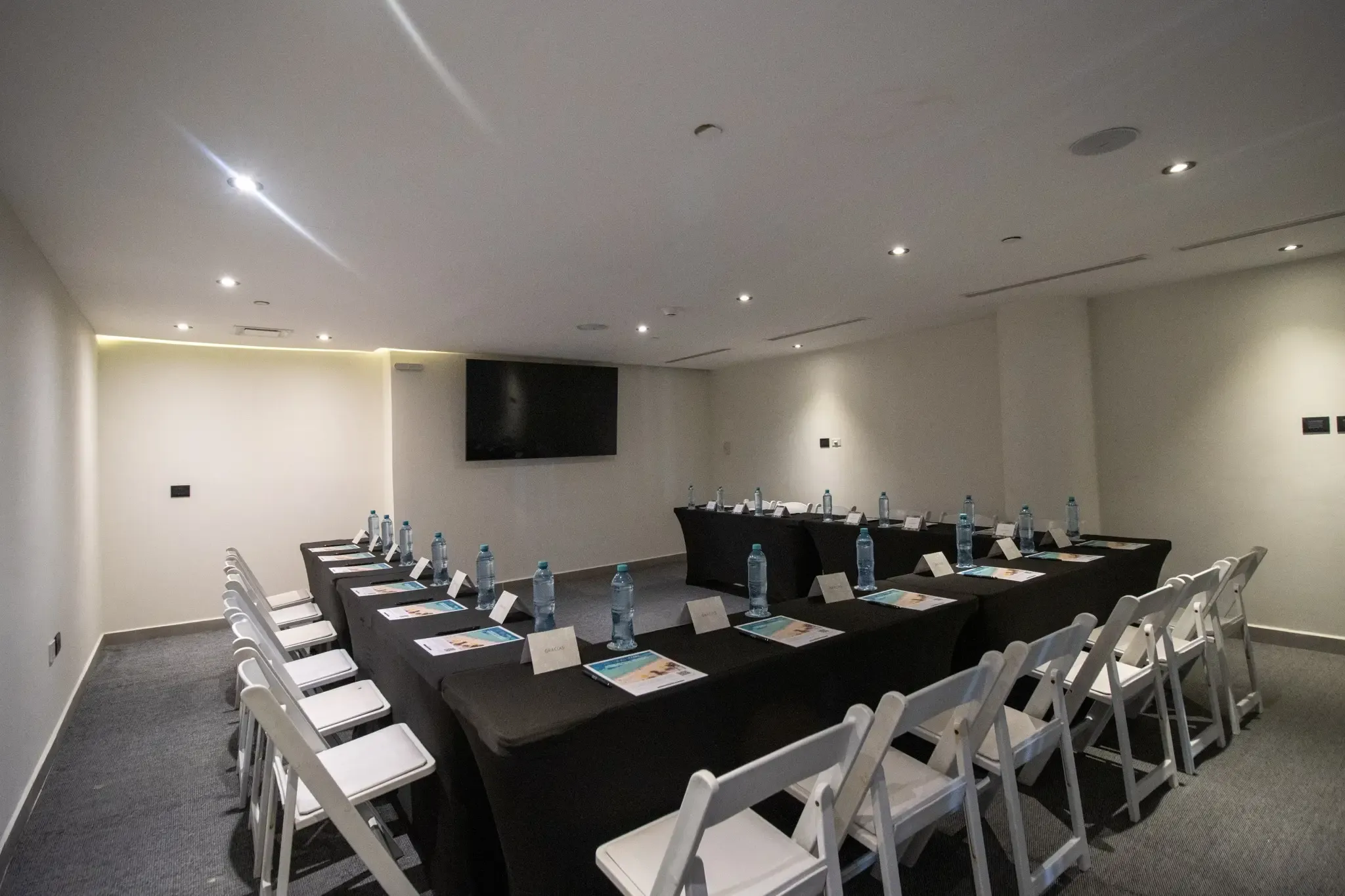 Sala de reuniones con mesas cubiertas de negro, sillas blancas y The Fives Corpo.