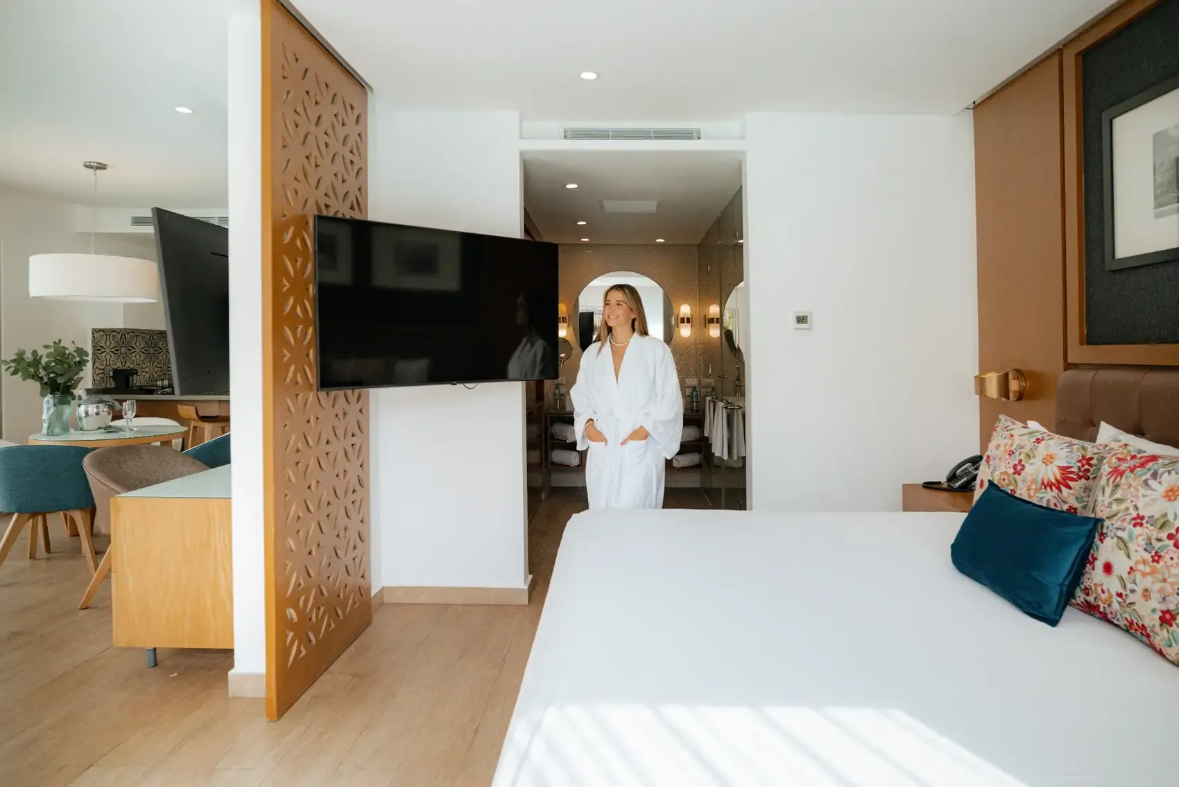 A woman in a white robe smiles in a modern hotel suite. The Fives Corpo
