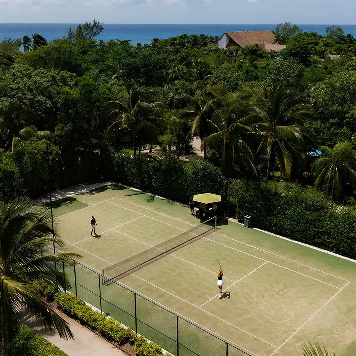 The Fives Corpo tennis court with players and Caribbean Sea views.