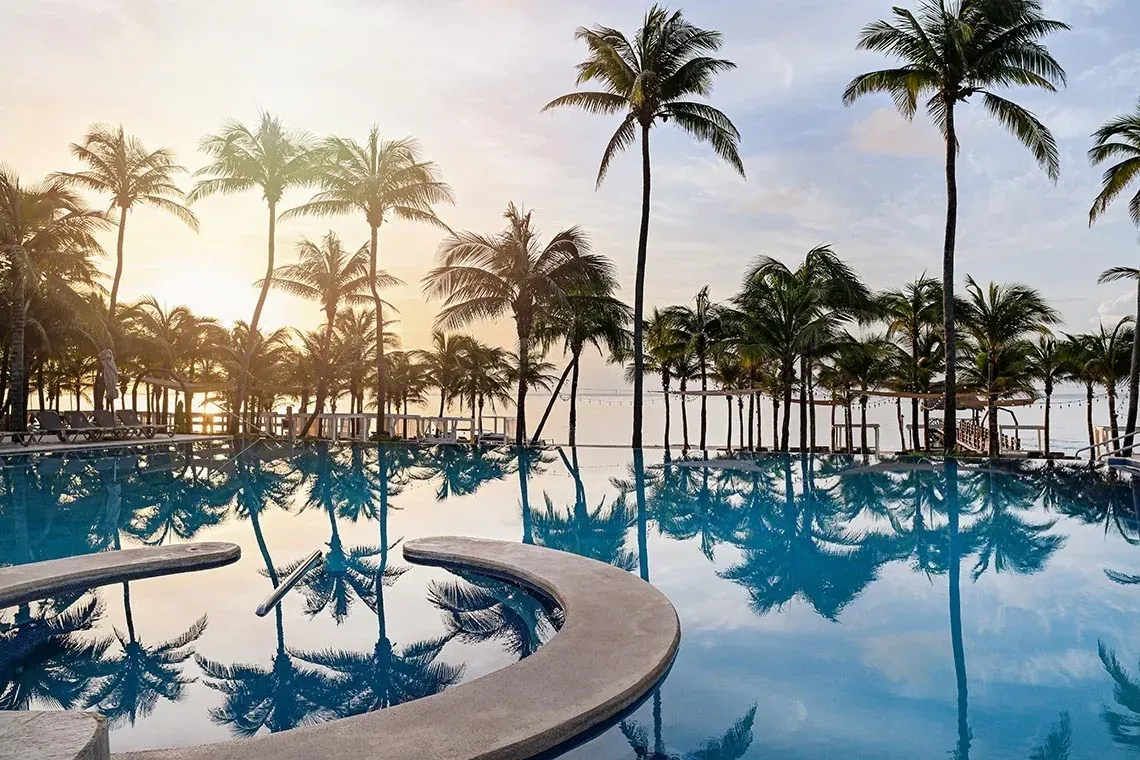 Piscina de The Fives Beach Hotel - Todo Incluido, México. Reflejos de palmeras al atardecer.