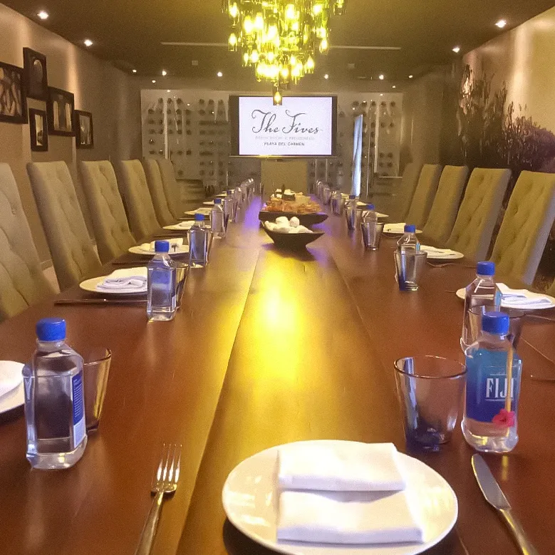 Elegant dining room setup at The Fives Corpo with a long table, chairs, and a projected logo.