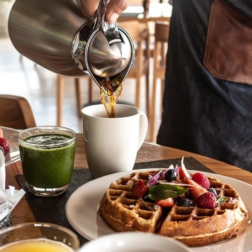 a person pouring coffee into a cup next to a plate of waffles