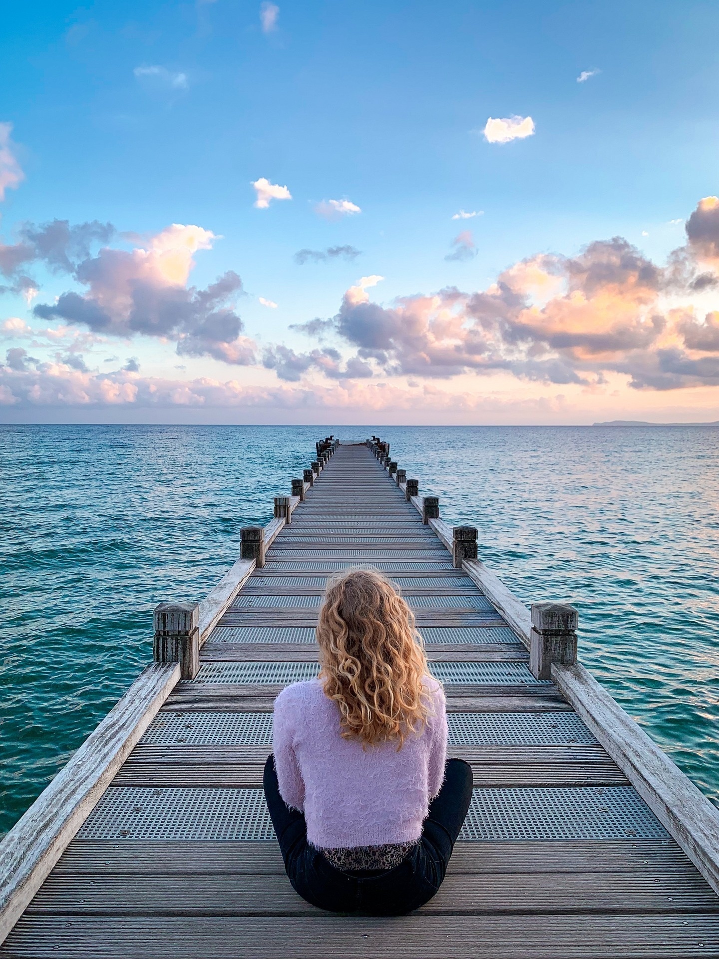 una mujer sentada en un muelle mirando al océano