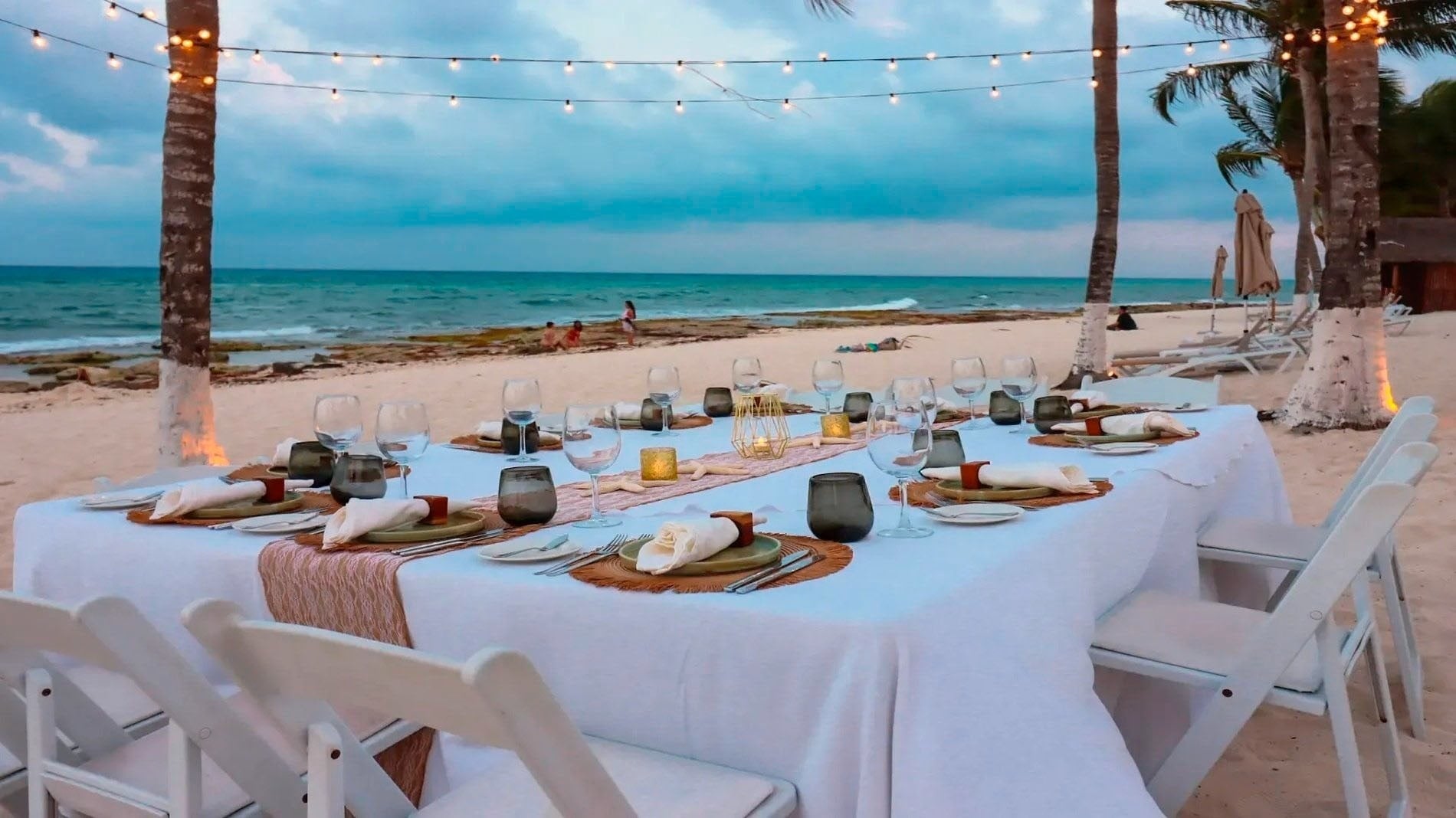 a table set up on the beach with plates and glasses