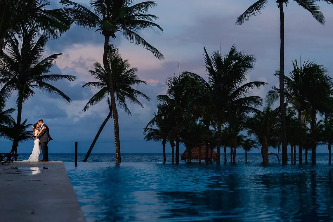 Couple kissing at The Fives Corpo resort with palm trees at dusk.