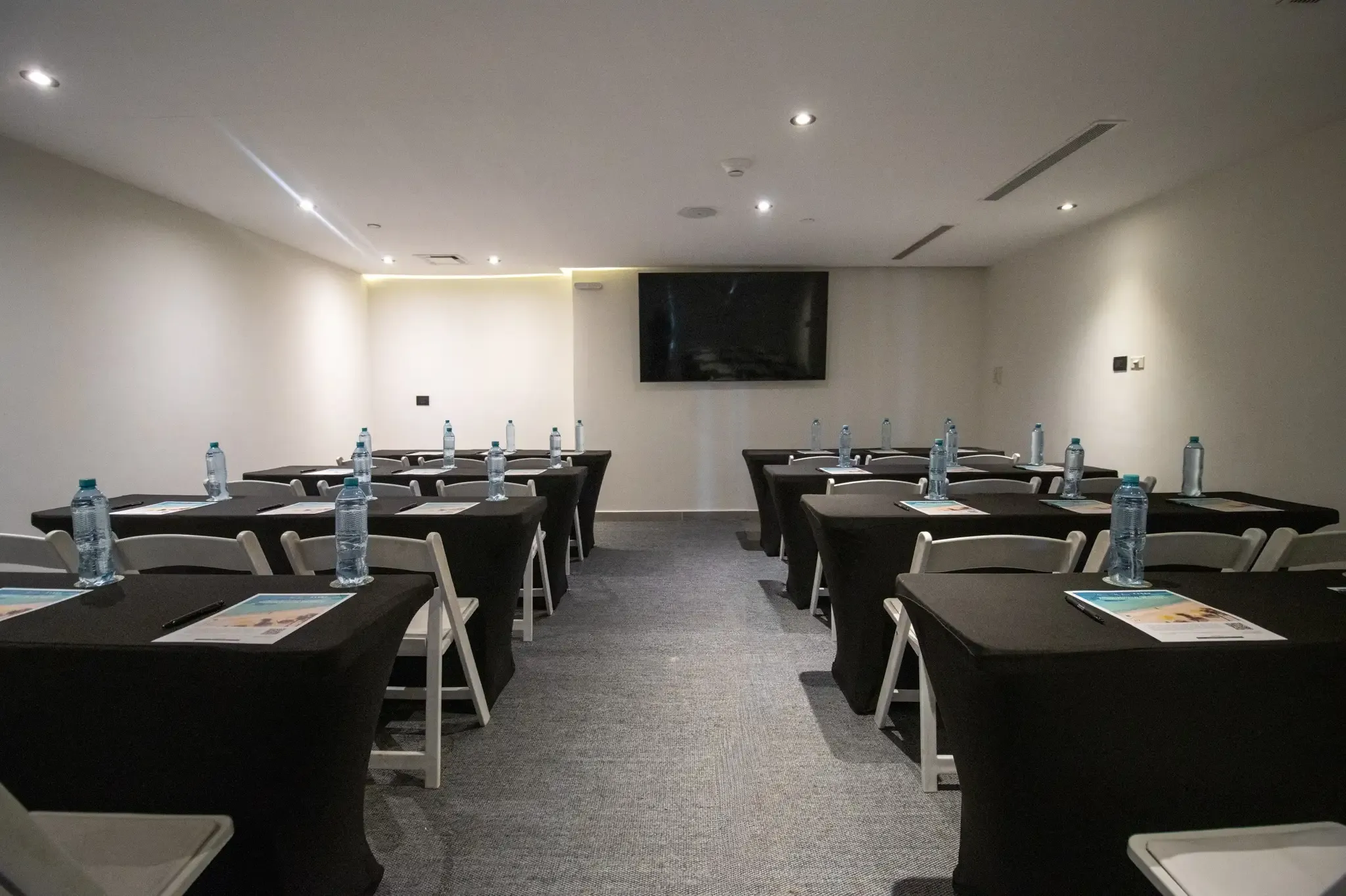 Salón de conferencias con mesas cubiertas de negro y botellas de agua, ideal para The Fives Corpo.