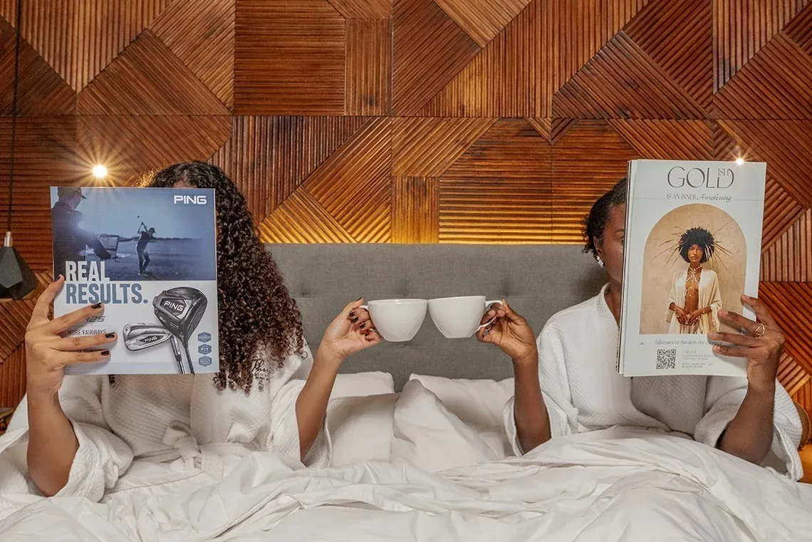 The Fives Downtown Hotel: Two women read magazines and drink coffee in bed.