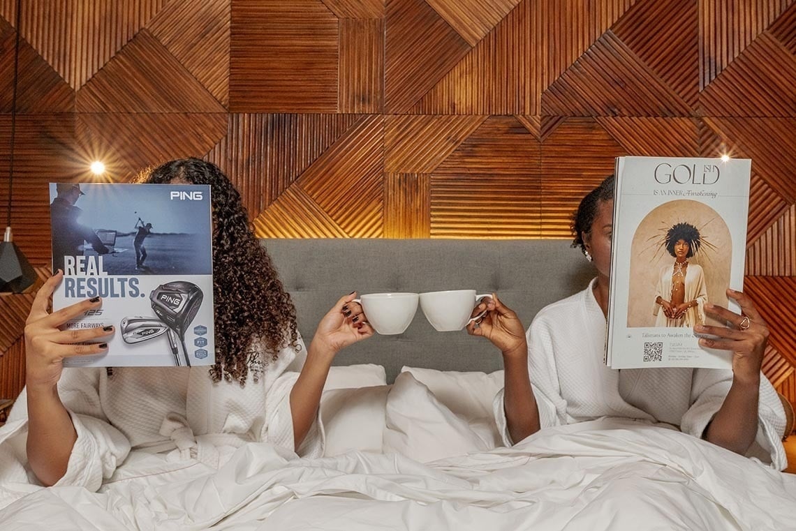 The Fives Downtown Hotel: Two women read magazines and drink coffee in bed.