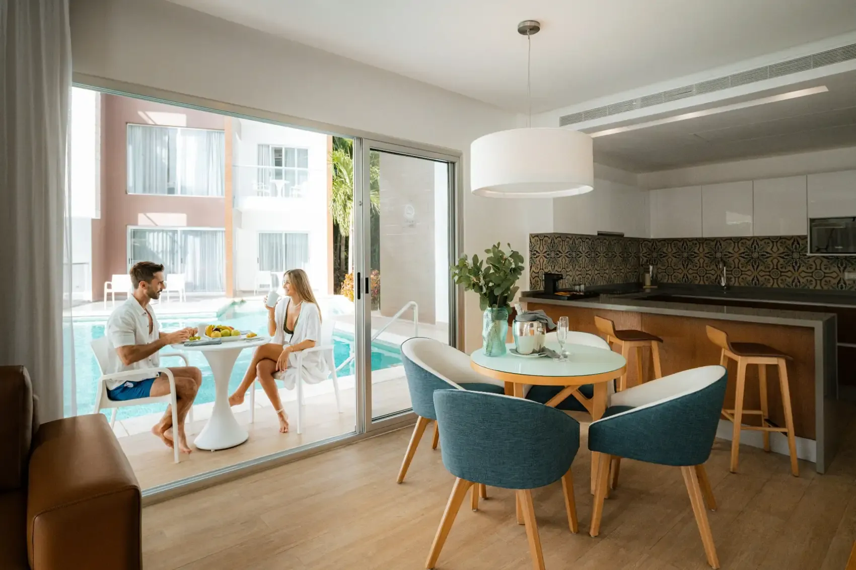 Couple enjoying breakfast by the pool at an The Fives Corpo suite with a modern kitchen.