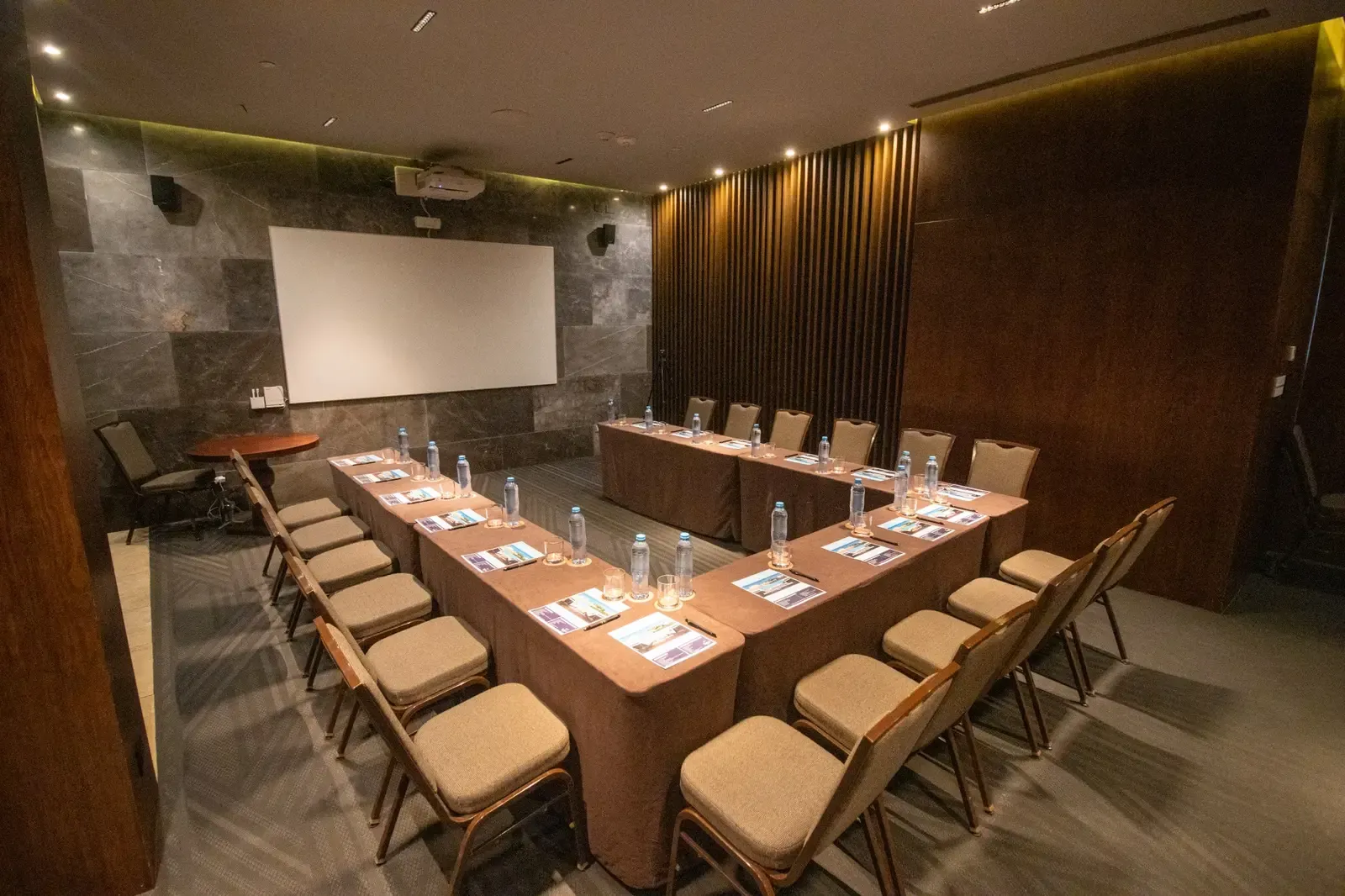 Modern U-shaped conference table setup with chairs, projector, and screen in a hotel meeting room. The Fives Corpo
