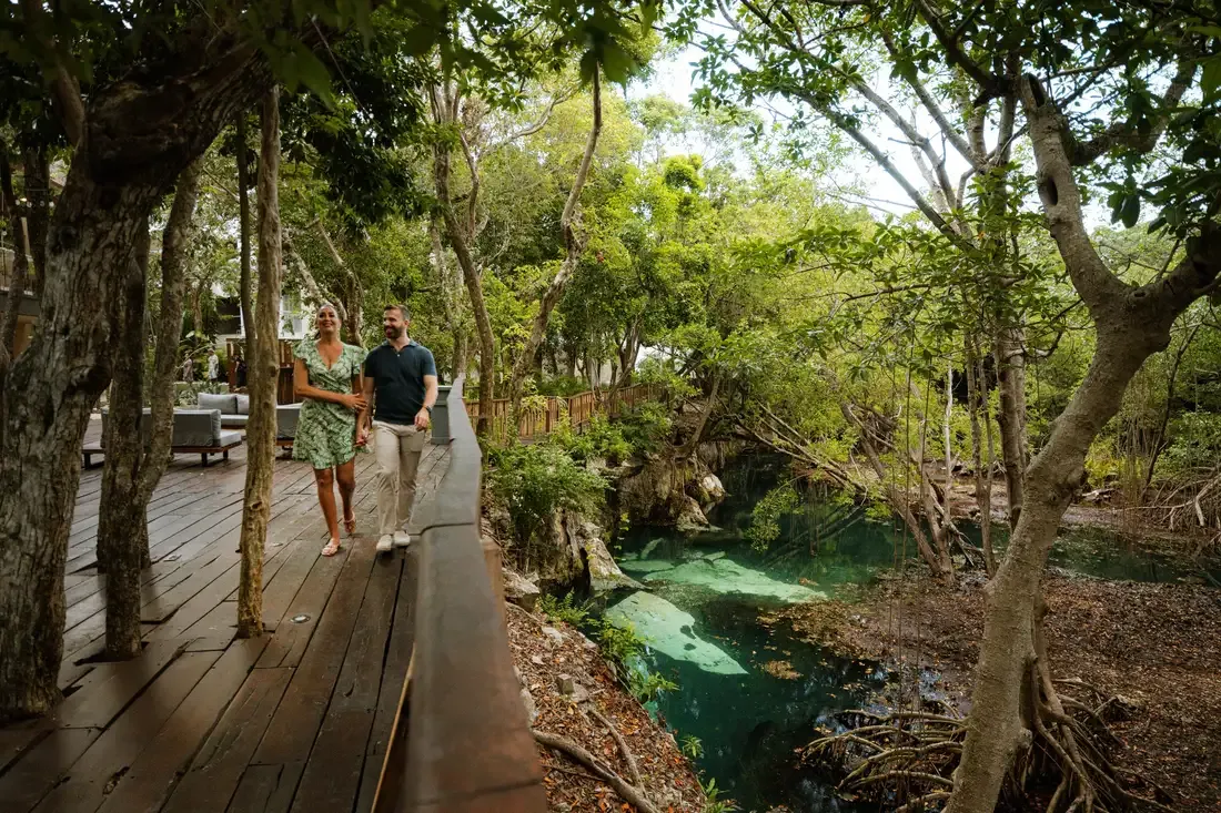 Couple walking on a wooden path next to a cenote at The Fives Corpo.
