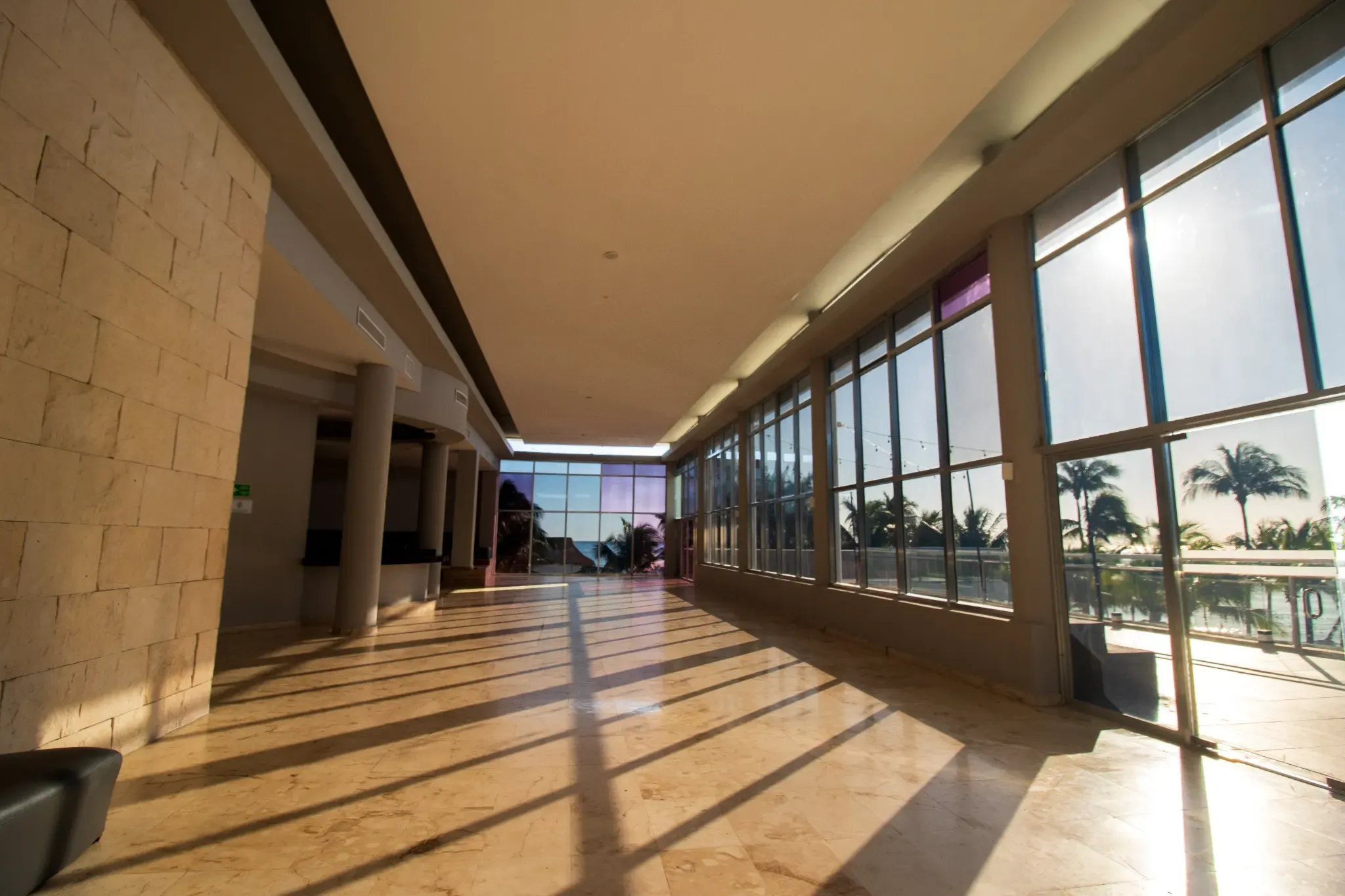 Sunlit hotel hallway with large windows offering ocean and palm tree views. The Fives Corpo