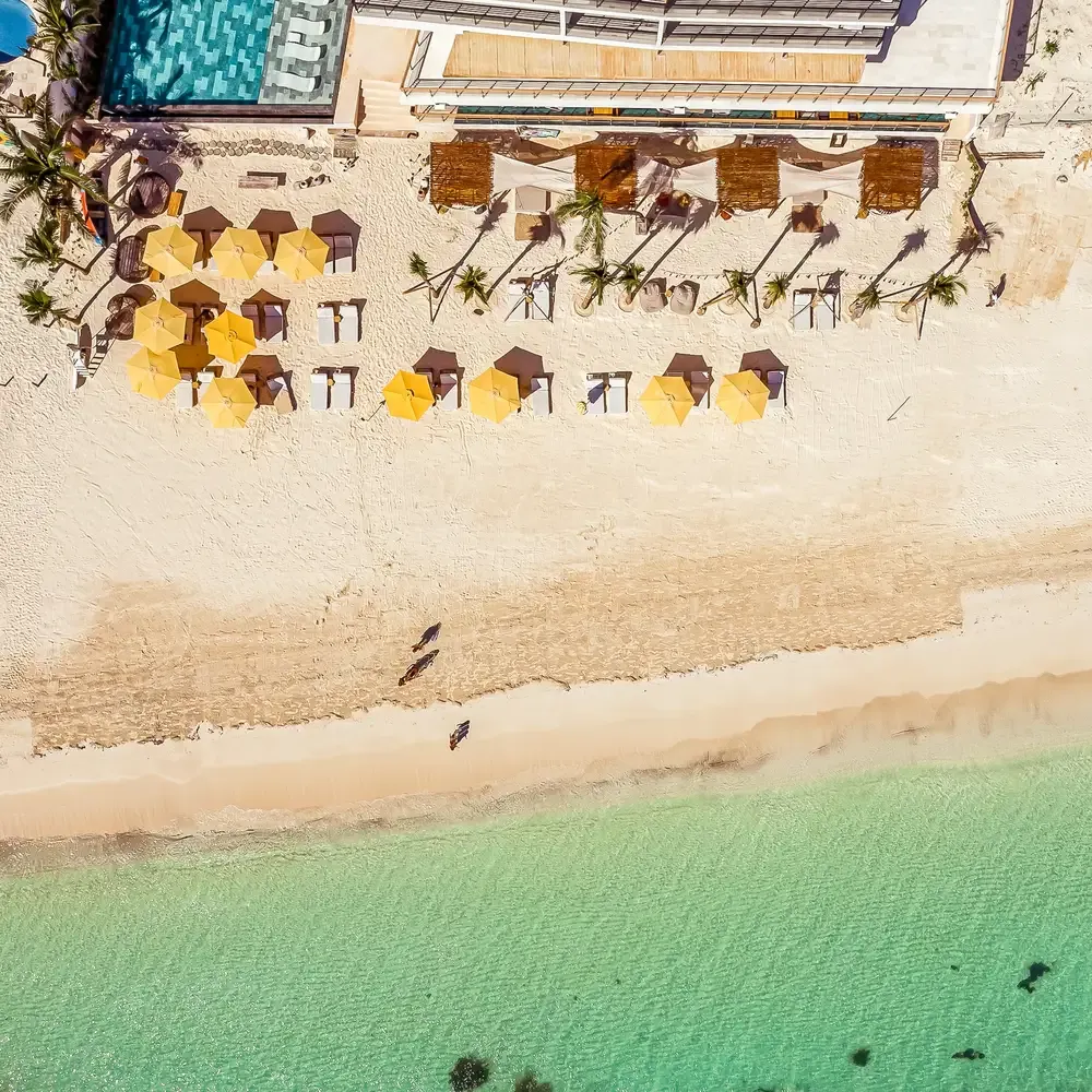 Luxury resort beach with yellow umbrellas, lounge chairs, pool and turquoise ocean. The Fives Corpo