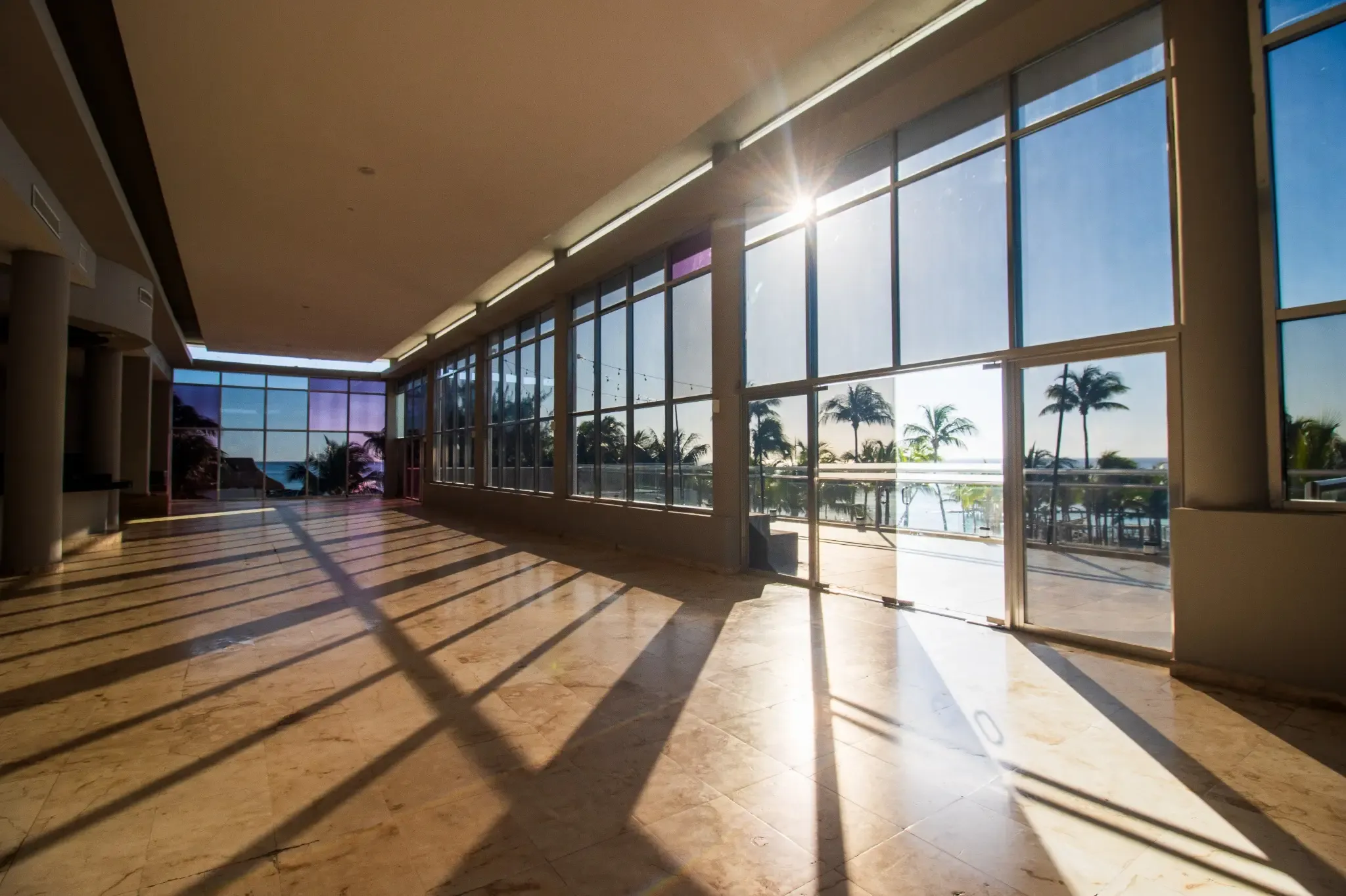 Bright sunlit indoor hotel lobby with ocean view and palm trees, ideal for events. The Fives Corpo