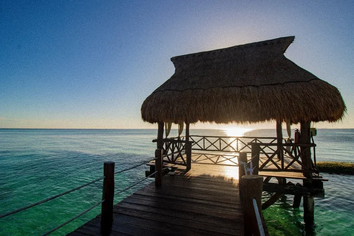 Oceanfront thatched-roof cabana and pier at sunrise, perfect for The Fives Corpo relaxation.