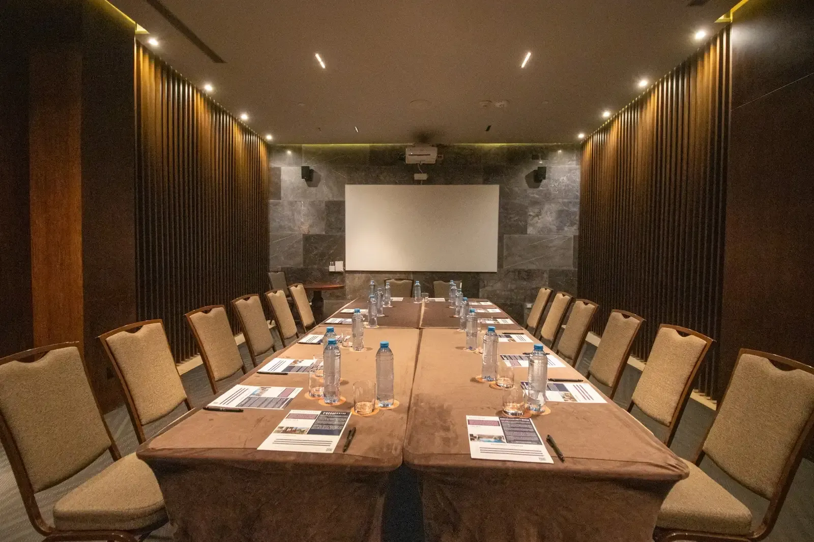 The Fives Corpo: Modern conference room with long table, chairs, projector screen, and water bottles.