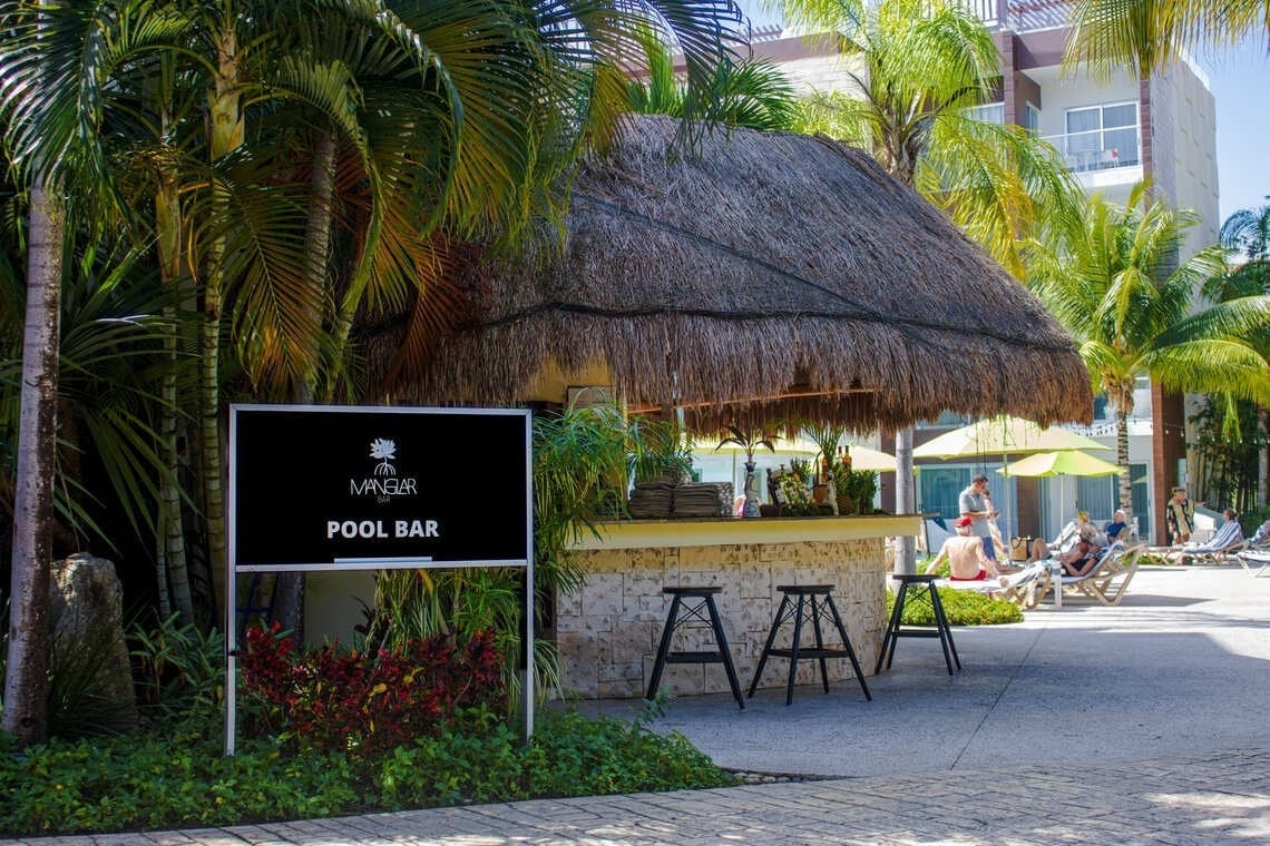 Manglar Pool Bar at The Fives Beach in Riviera Maya, thatched palapa bar surrounded by palm trees and lounge chairs near the pool.