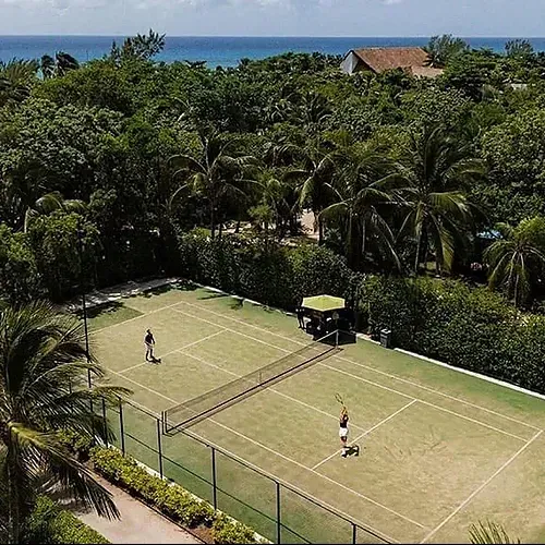 Players on The Fives Corpo tennis court, surrounded by lush greenery and the sea.