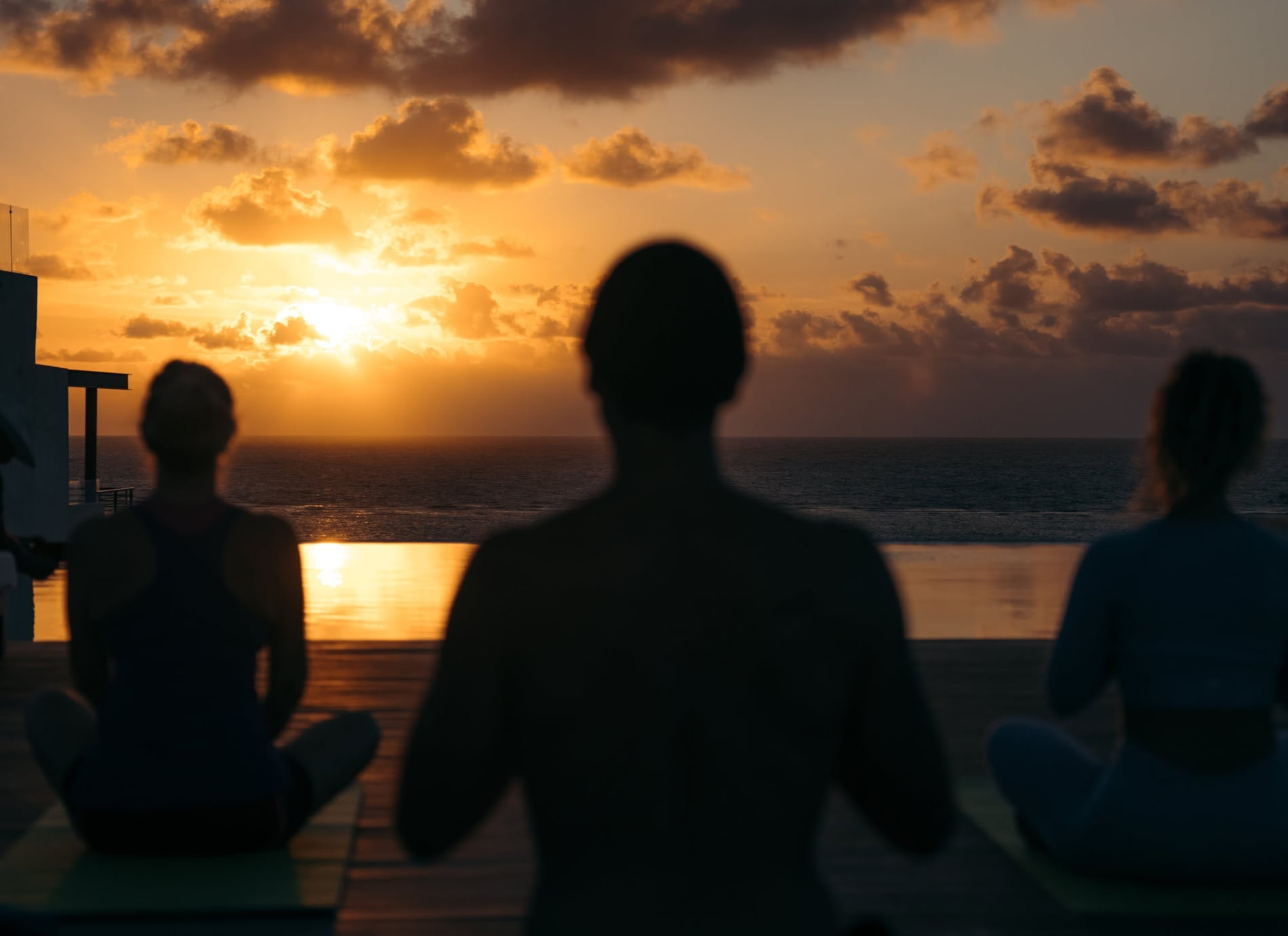 Rooftop sunset yoga at a hotel with ocean views and an infinity pool, with silhouetted guests.