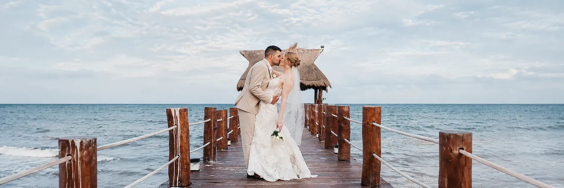 Newlywed couple on a beach with a pier and thatched-roof gazebo, perfect for a destination wedding All Senses Weddings in Rivera Maya | The Fives Hotels.