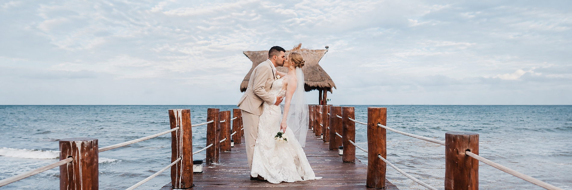 Newlywed couple on a beach with a pier and thatched-roof gazebo, perfect for a destination wedding All Senses Weddings in Rivera Maya | The Fives Hotels.