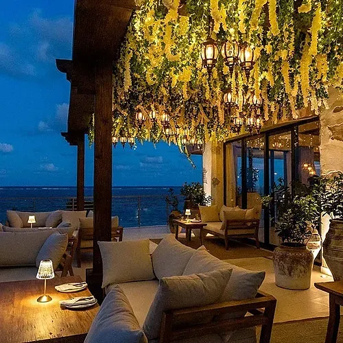 The Fives Corpo oceanfront terrace at twilight with glowing lanterns and plush seating.