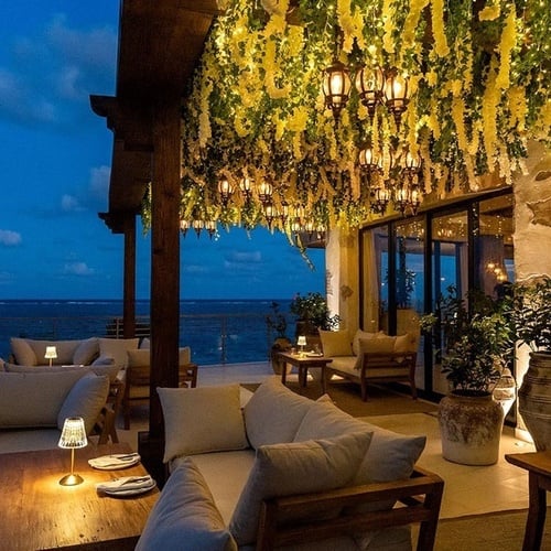 a balcony with a couch and tables with a view of the ocean