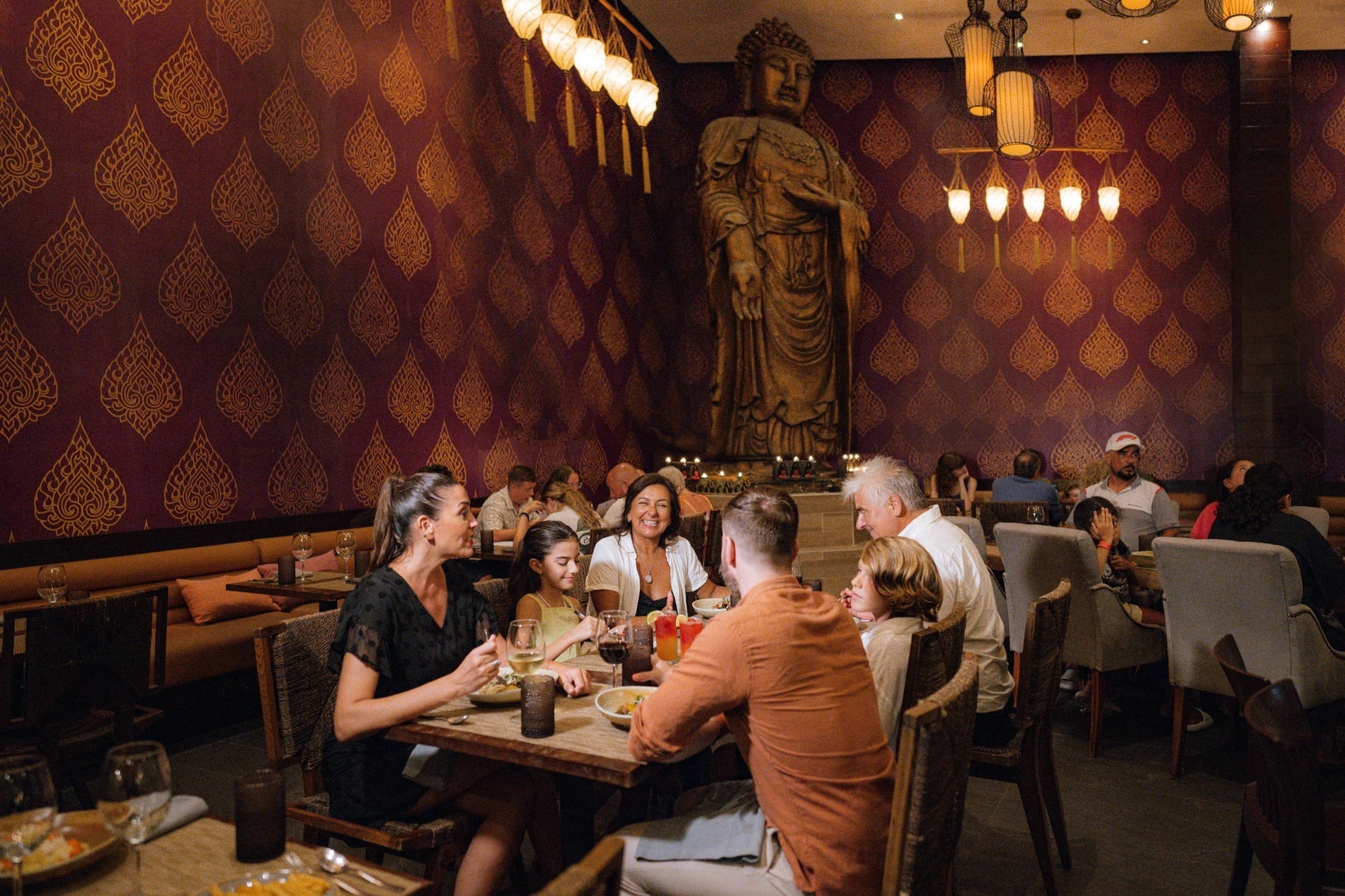 Hotel restaurant guests enjoy an inviting Thai dining experience with a prominent Buddha statue and patterned walls.
