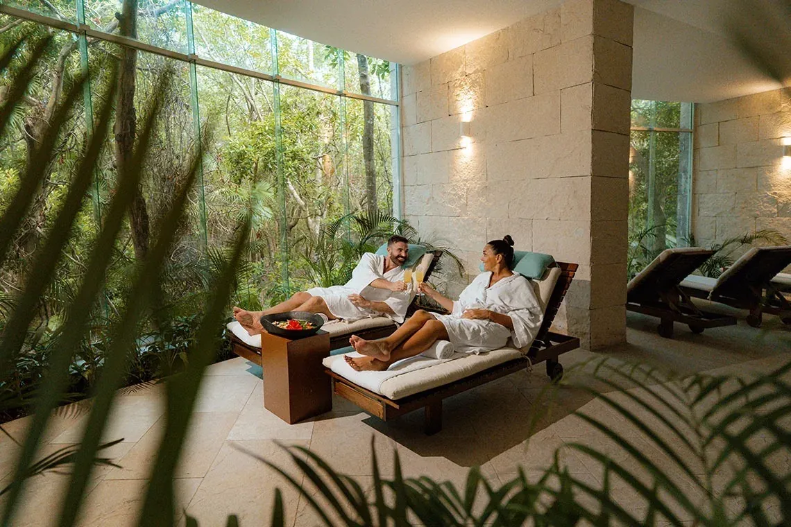 Pareja en The Fives Corpo relajándose en el spa, brindando con champagne y vistas a la selva.