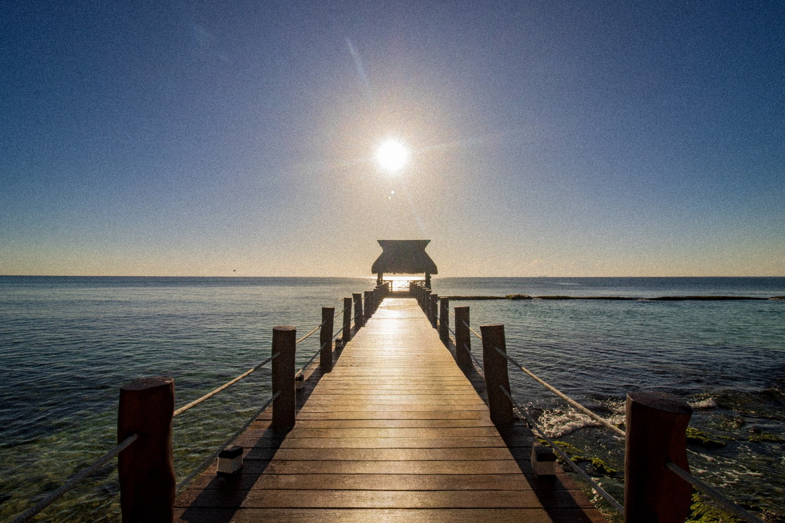 Wooden pier leading to a thatched-roof gazebo over turquoise water at a The Fives Corpo.