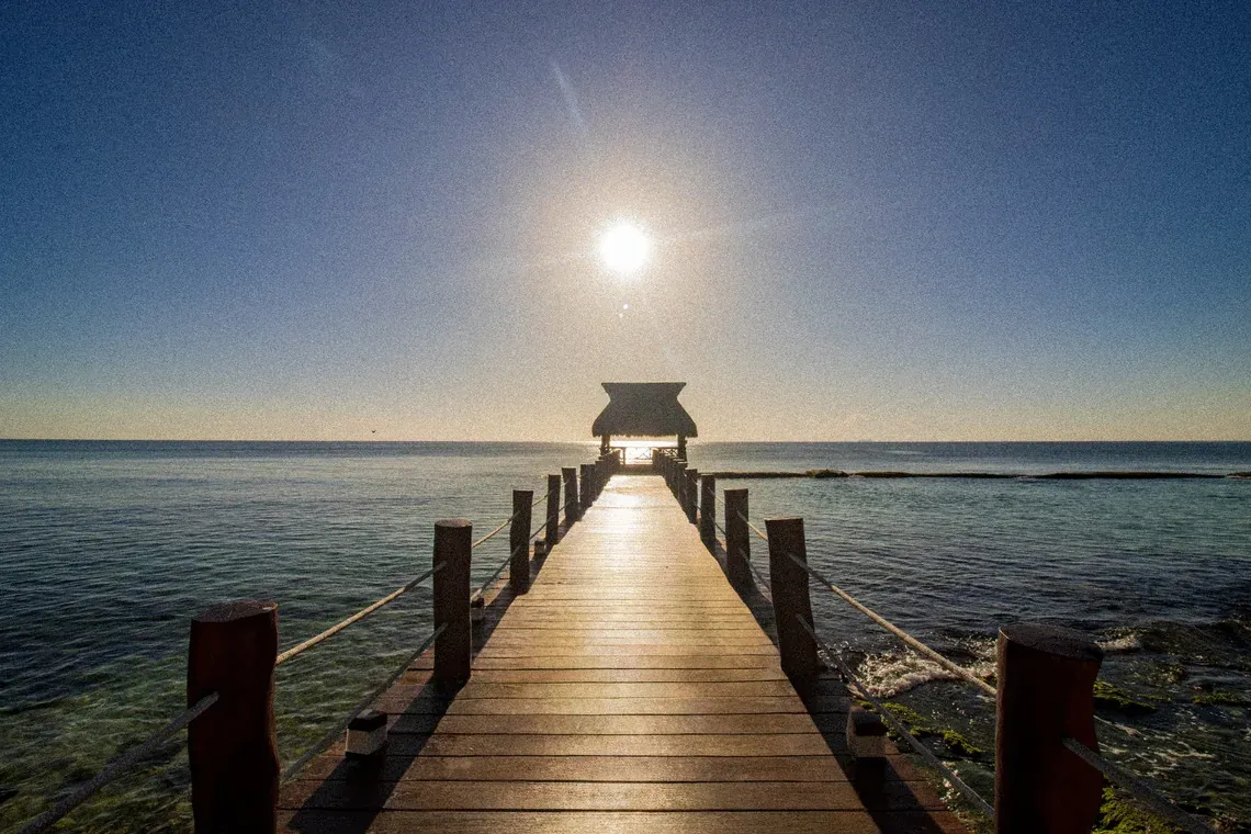 Wooden pier leading to a thatched-roof gazebo over turquoise water at a The Fives Corpo.