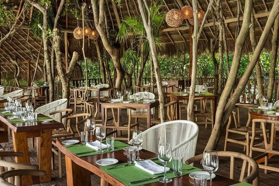 The Fives Corpo resort's rustic outdoor dining area with natural wood tables and chairs amidst lush greenery.