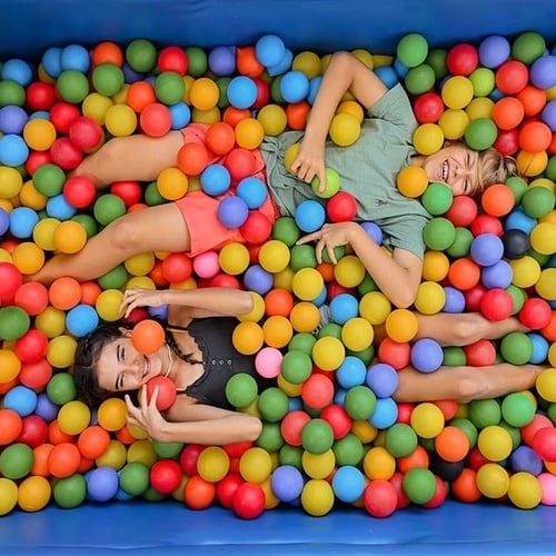 a boy and a girl are laying in a ball pit