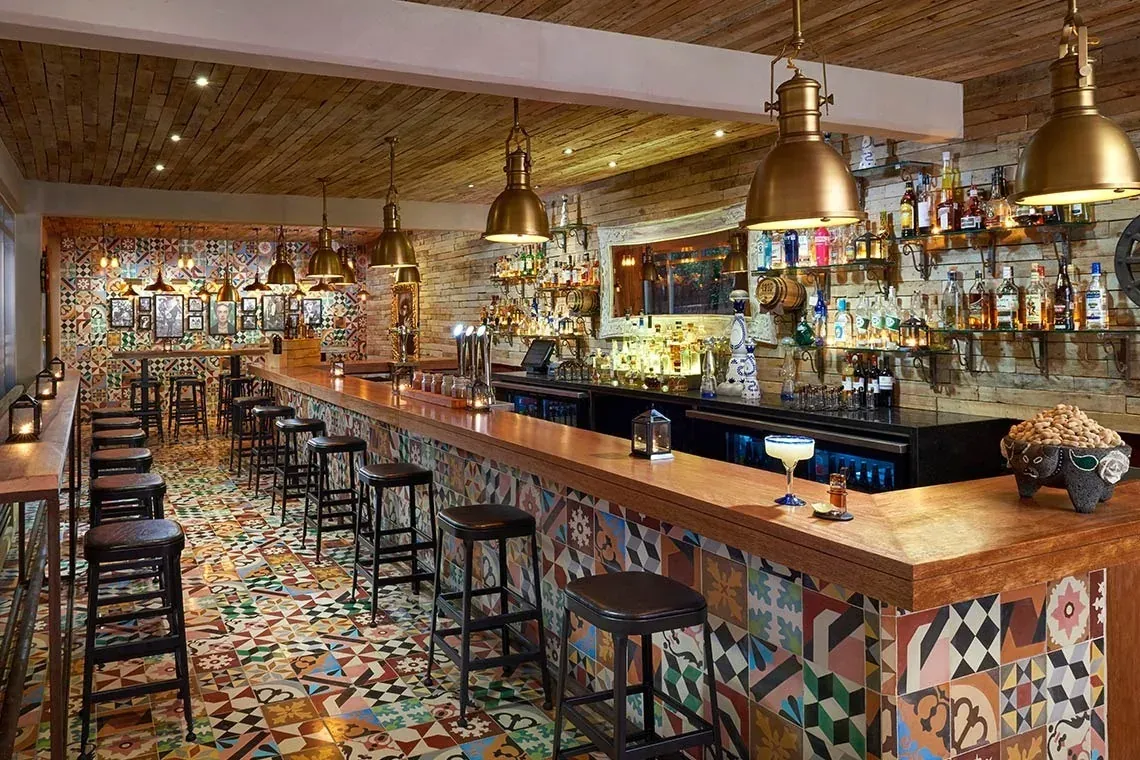 Bar vibrante en The Fives Corpo con azulejos coloridos, taburetes y licores.