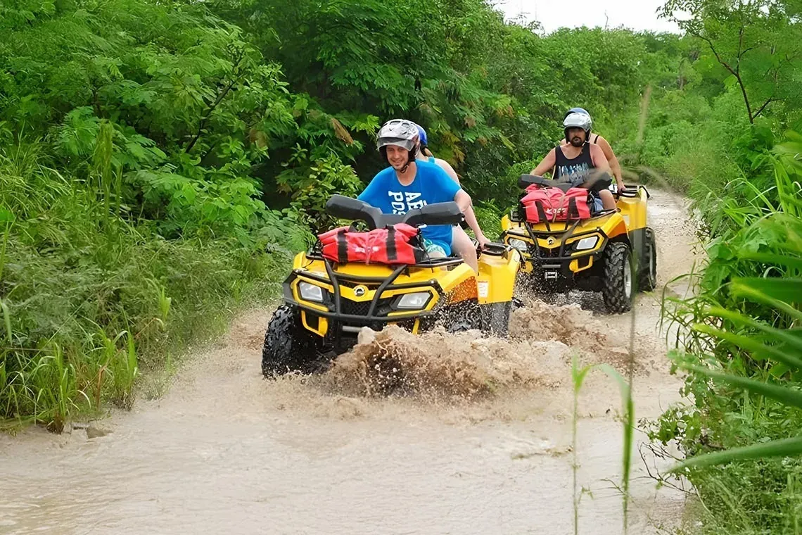 Off-road adventure at The Fives Corpo: two people on yellow ATVs splash through a muddy path.