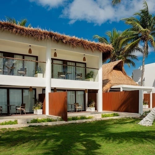a white house with a thatched roof sits next to a palm tree