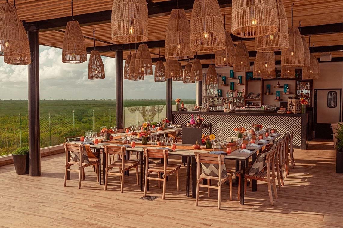 The Fives Corpo hotel bar with set tables and lush landscape view.