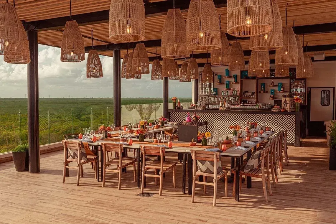 The Fives Corpo hotel bar with set tables and lush landscape view.
